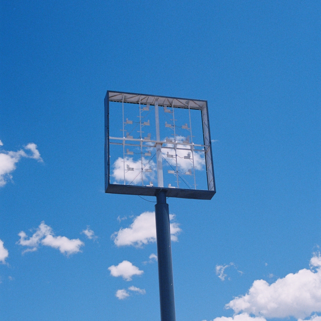 a transparent billboard frame revealing clouds in the sky. album cover for maysayer single "light leaks through the curtain"